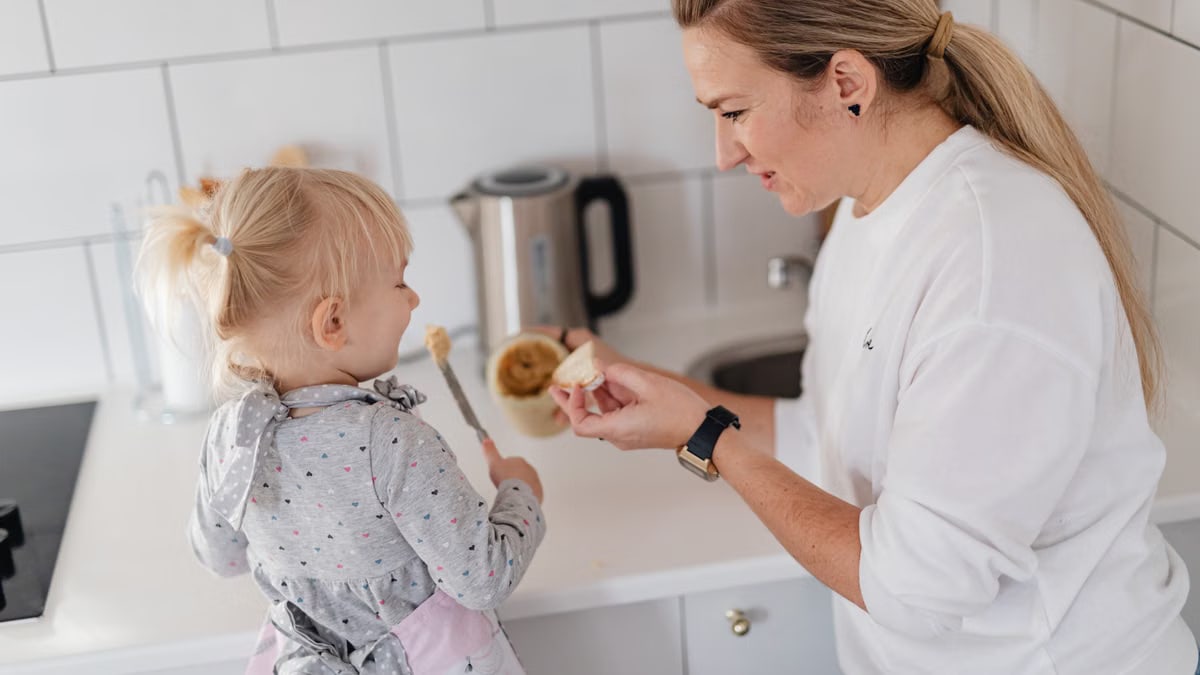 A mother and her young daughter interact while preparing food in a modern kitchen.